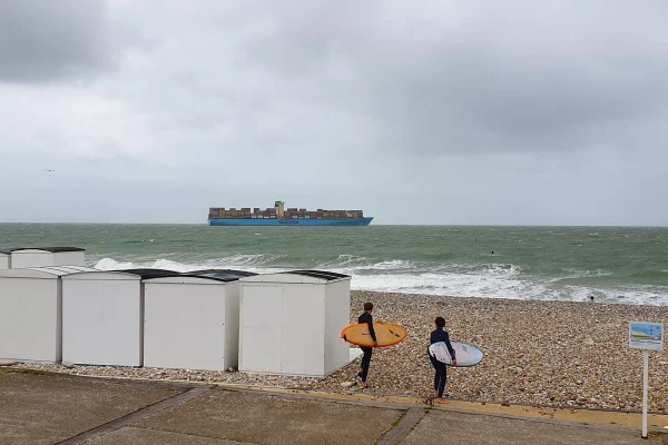 Jeunes portant une planche de surf devant une mer agitée au Havre
